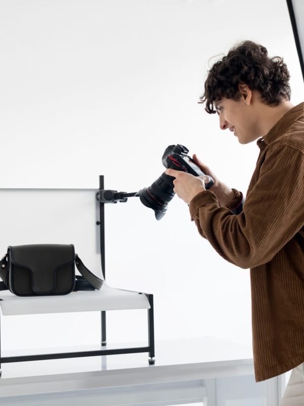 From vision to reality. Young photographer guy making content photos for modern shop, photographing female bags, working in professional modern photostudio